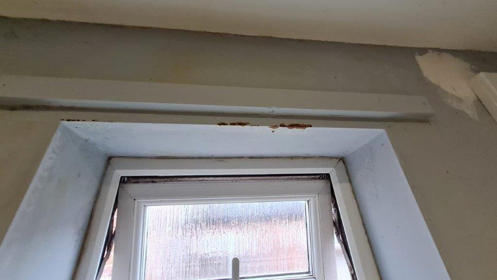 Damp staining and paint failure around a window reveal
