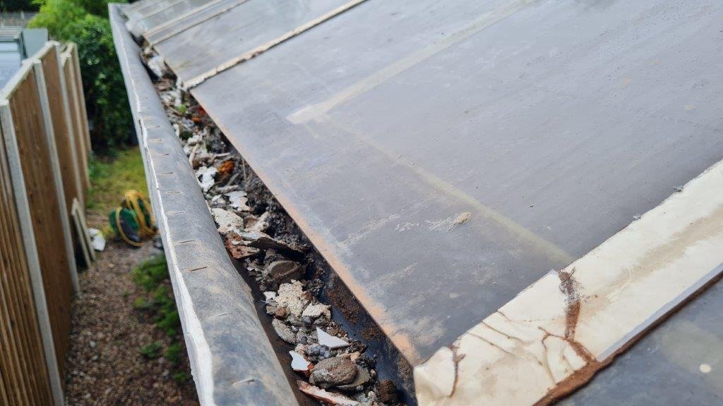 Blocked guttering full of moss and debris on a pitched roof
